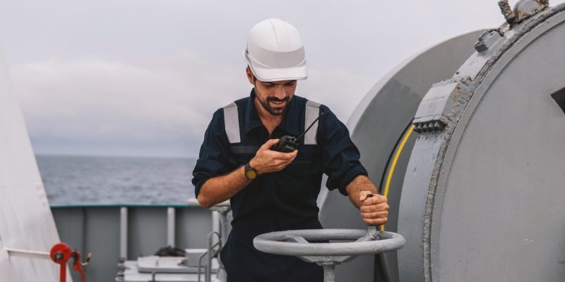 Marine Deck Officer or Chief mate on deck of vessel or ship . He holds VHF walkie-talkie radio in hands. Ship communication
