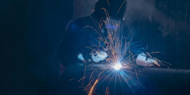 Professional welder and mask welding metal pipe on the industrial table.